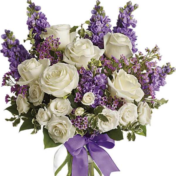 White roses and purple flowers in a glass vase with a purple ribbon