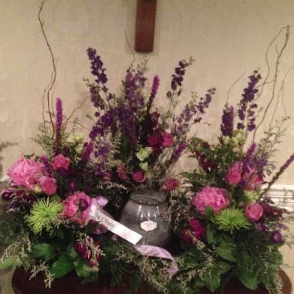 Large purple and pink floral funeral arrangement with a vase centerpiece