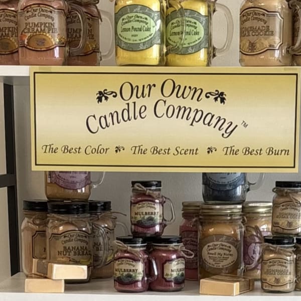 Shelf display of scented candles in mason jars with a company sign.