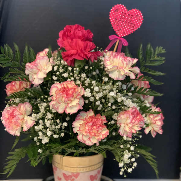 Pink and white carnations in a decorated pot with a heart pick