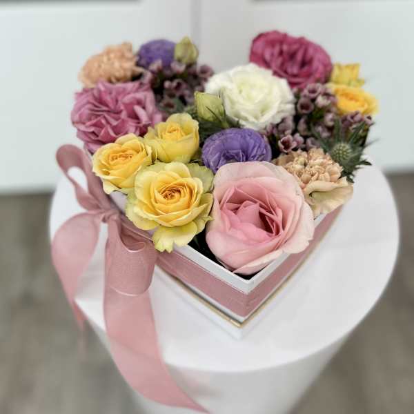 Heart-shaped box of pastel roses and carnations with a pink ribbon