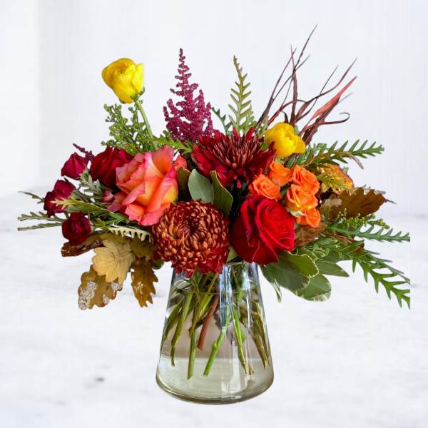 Mixed bouquet of red, orange, and yellow flowers in a clear glass vase