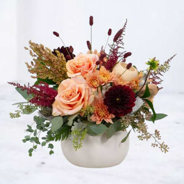 Peach roses and burgundy flowers arranged in a white vase