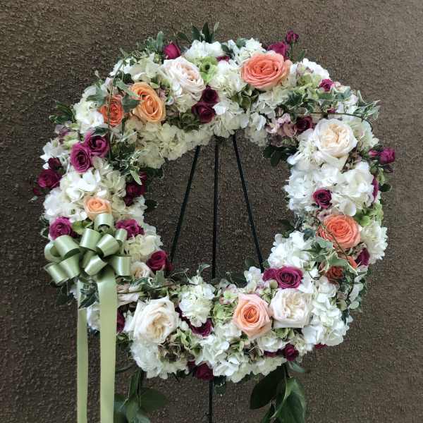 Floral wreath with white, peach, and magenta roses on a stand