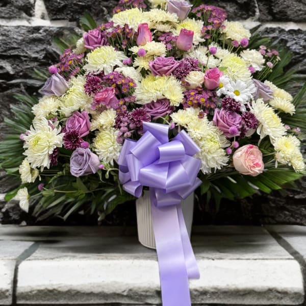 Lavender and white floral arrangement with a purple ribbon in a white vase