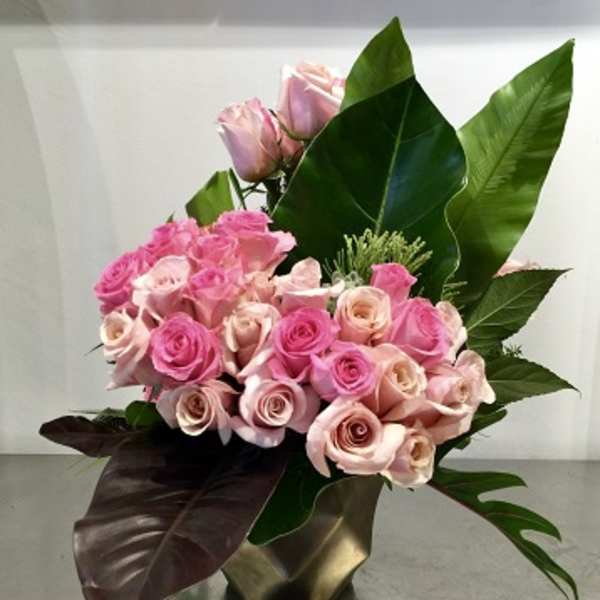 Pink roses arranged in a gold vase with large tropical leaves