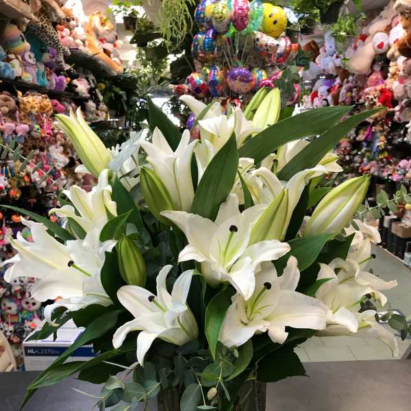 White lilies arranged in a clear glass vase with greenery