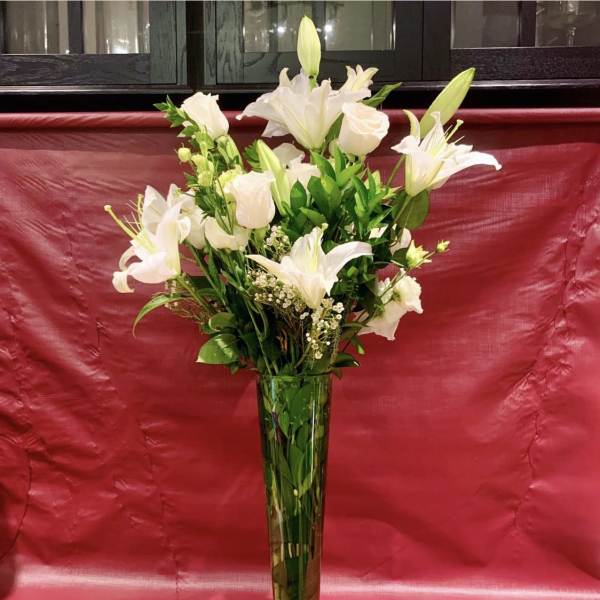 White lilies and roses arranged in a tall glass vase