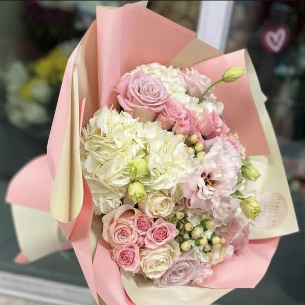 Pink and white bouquet of roses, hydrangeas, and lisianthus in pastel wrap