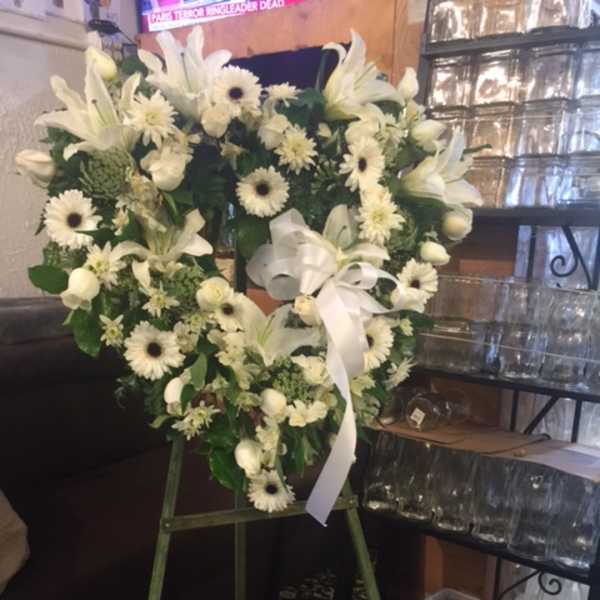 White floral wreath on a stand with a white ribbon bow