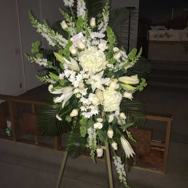 Tall white funeral spray on an easel with lilies and roses