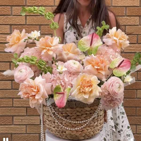 Large pastel floral arrangement in a woven basket with pearl strands