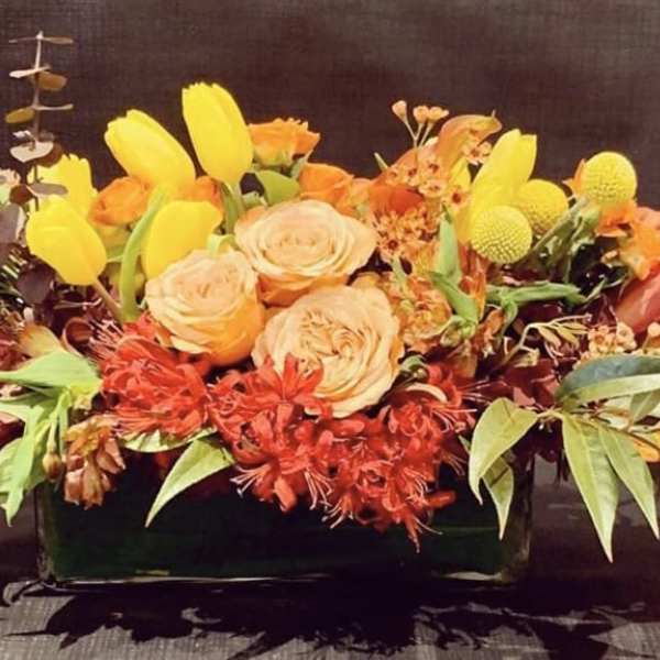 Orange and yellow floral arrangement in a low rectangular container