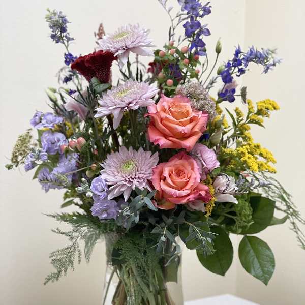 Mixed bouquet of pink roses, lavender blooms, and blue flowers in a glass vase
