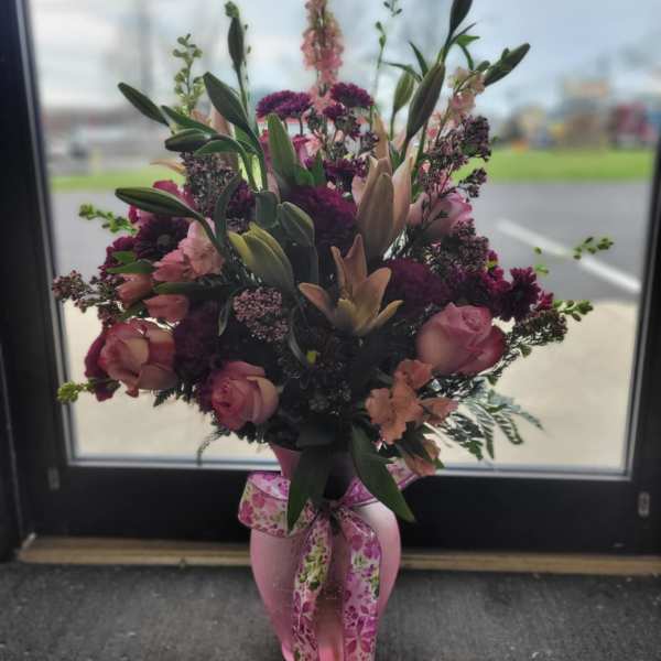 Pink and purple floral arrangement in a pink vase with a ribbon