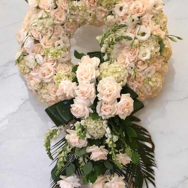 Large floral wreath of pale pink roses and cream blooms with dark green ribbon