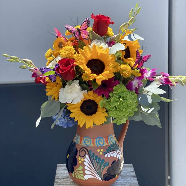 Bright mixed bouquet with sunflowers, roses, orchids, and butterflies in a painted vase