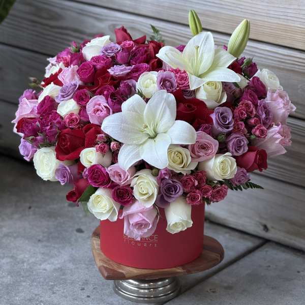 Large bouquet of pink, red, and white roses with white lilies in a red box