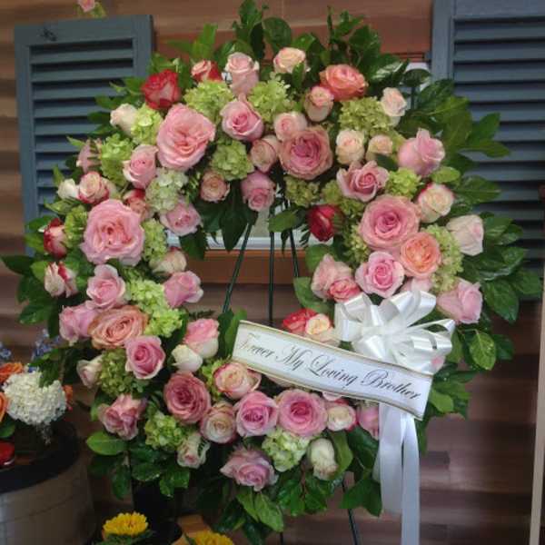 Pink rose funeral wreath with a white ribbon on a stand