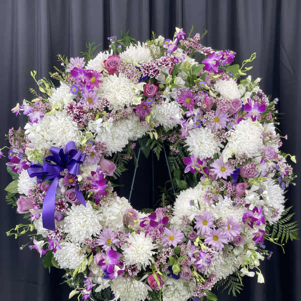 Large purple and white floral wreath on a stand with a ribbon bow