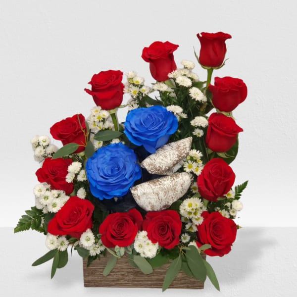 Red and blue roses with small white blooms and silver bird accents in a wooden box arrangement