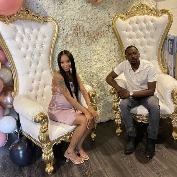 Balloon backdrop with two ornate white-and-gold chairs and seated couple