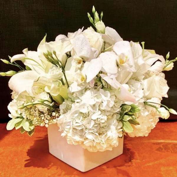 White floral arrangement in a square vase with orchids and hydrangeas