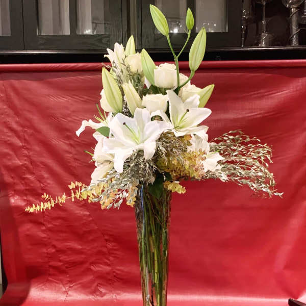 Tall white lily and rose arrangement in a clear glass vase