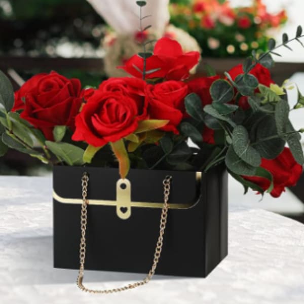 Red roses arranged in a black handbag-style box with gold chain handles.