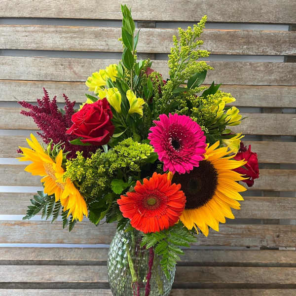 Mixed bouquet of sunflowers, gerbera daisies, and roses in a glass vase