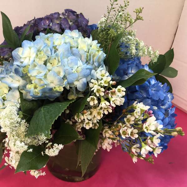Blue and purple hydrangea bouquet with white filler flowers in a vase