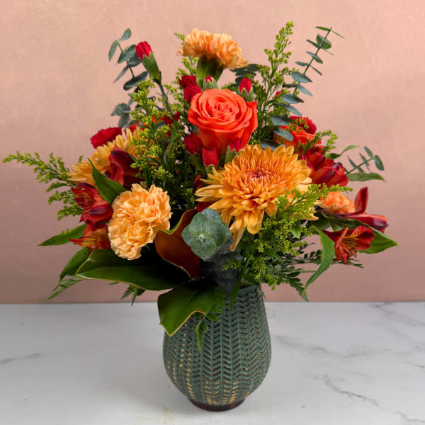 Orange and red mixed flower arrangement in a green vase