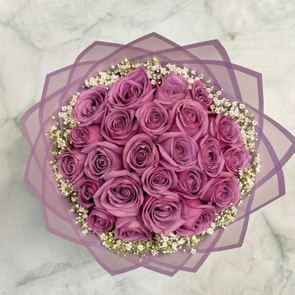 Round bouquet of purple roses with white filler flowers wrapped in lavender paper