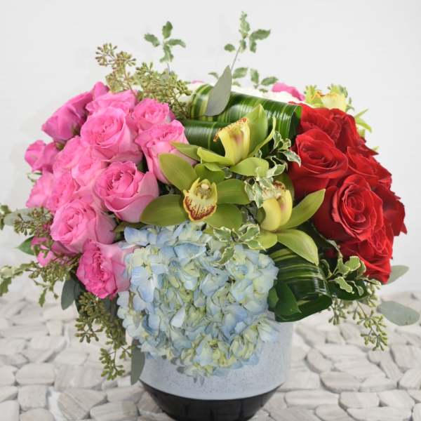 Pink and red roses with blue hydrangea and green orchids in a vase