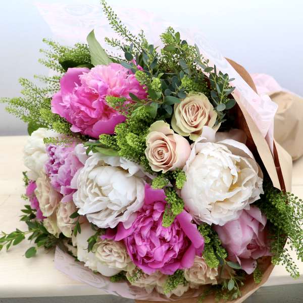 Hand-tied bouquet of pink peonies and cream roses wrapped in kraft paper