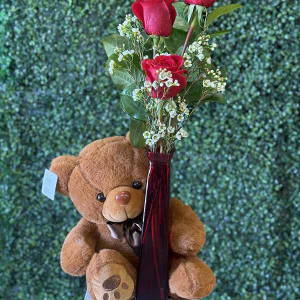 Red roses in a tall vase with a teddy bear