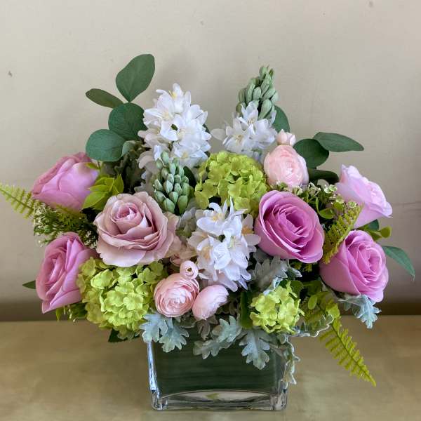 Low arrangement of pink roses, green hydrangeas, and white hyacinths in a clear glass rectangular vase
