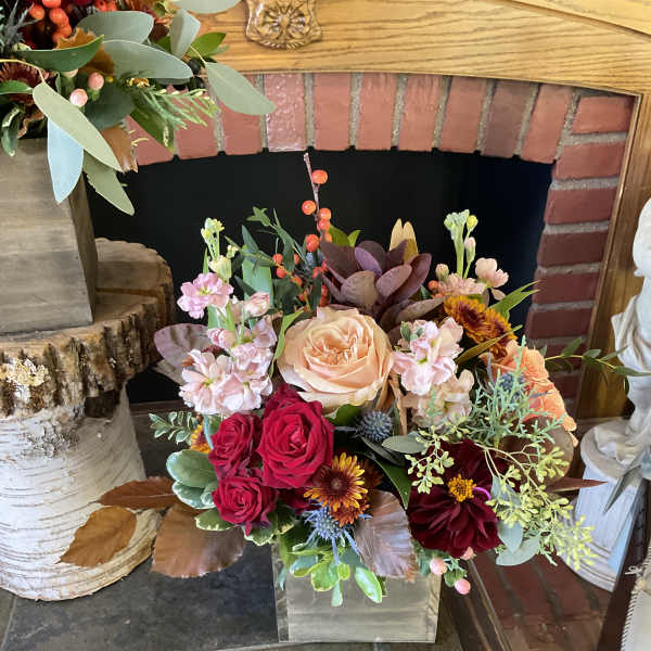 Mixed bouquet in a clear square vase with peach, red, and burgundy blooms