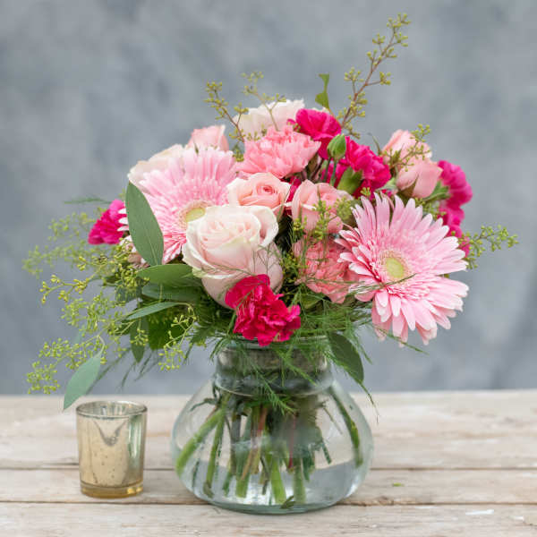 Pink and white bouquet in a glass vase with a small candle beside it