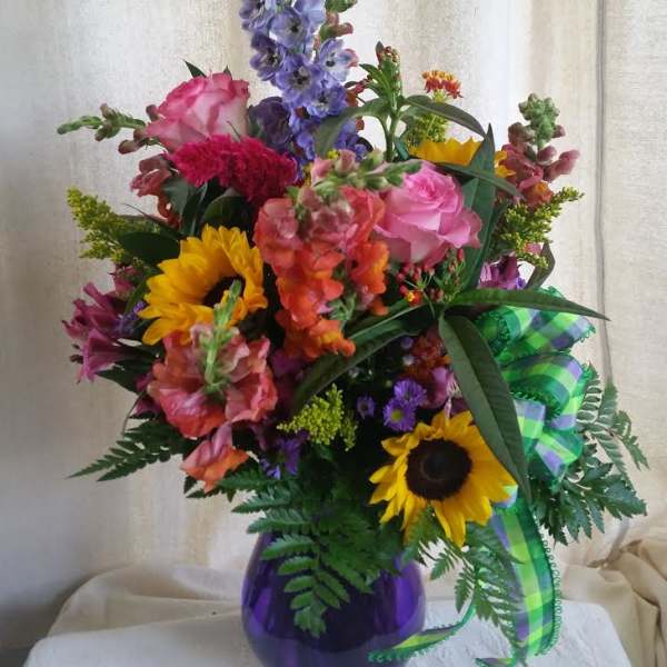 Mixed bouquet in a purple vase with sunflowers, roses, and purple spikes