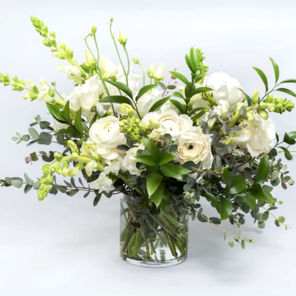 White floral arrangement in a clear glass vase with green foliage