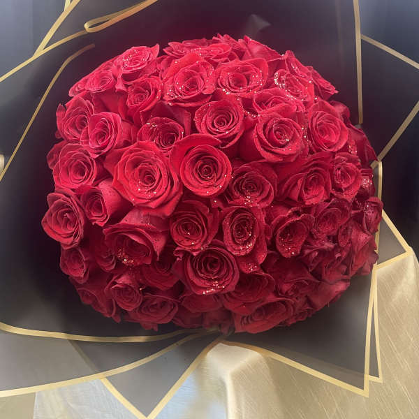 Round bouquet of red roses wrapped in black and gold paper