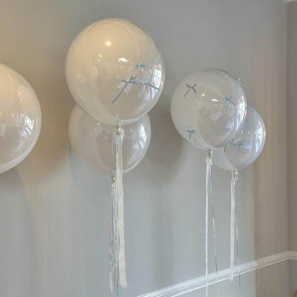 Clear balloons with pale blue ribbons and long white streamers against a wall