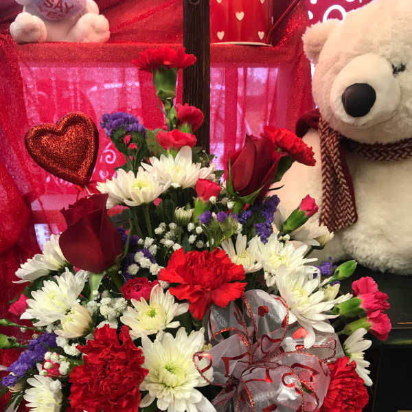 Red and white flower arrangement with a teddy bear and heart decorations