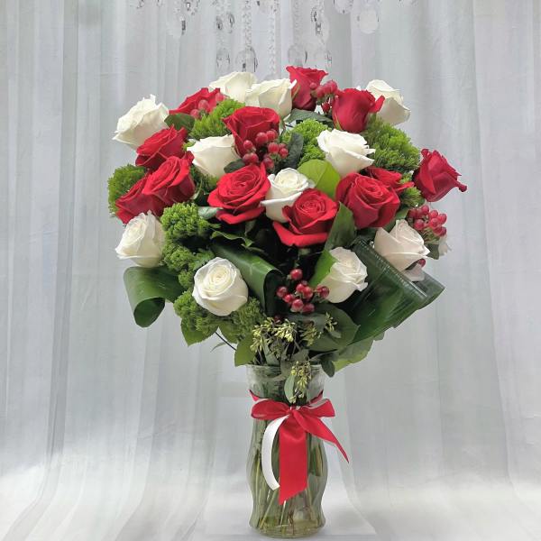 Red and white roses in a glass vase with a red ribbon