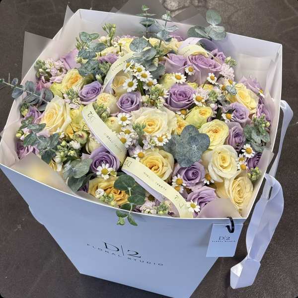 Bouquet of lavender and pale yellow roses with small white daisies in a gift box