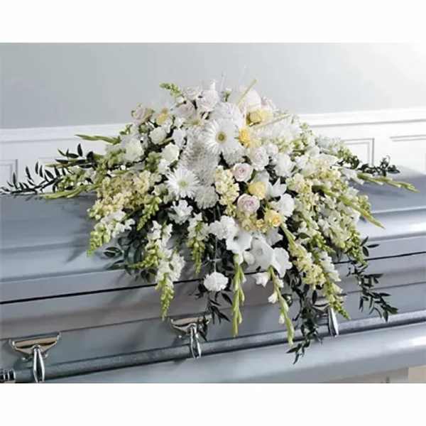 White floral casket spray with cascading greenery on a gray casket