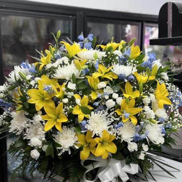 Large bouquet of yellow lilies, white chrysanthemums, and blue accents with a white ribbon