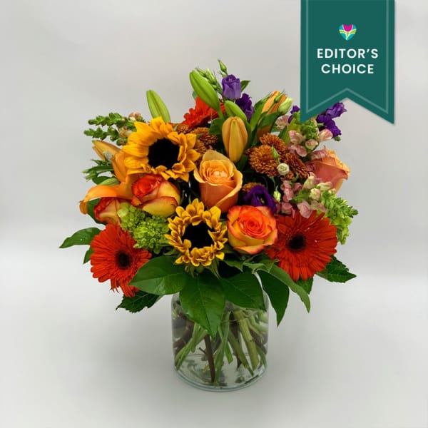 Mixed bouquet of sunflowers, roses, lilies, and gerbera daisies in a glass vase