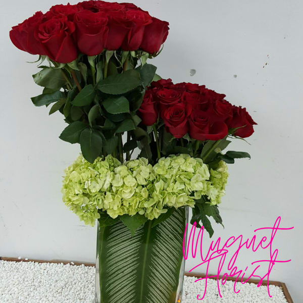 Red roses and pale green hydrangeas in a tall glass vase